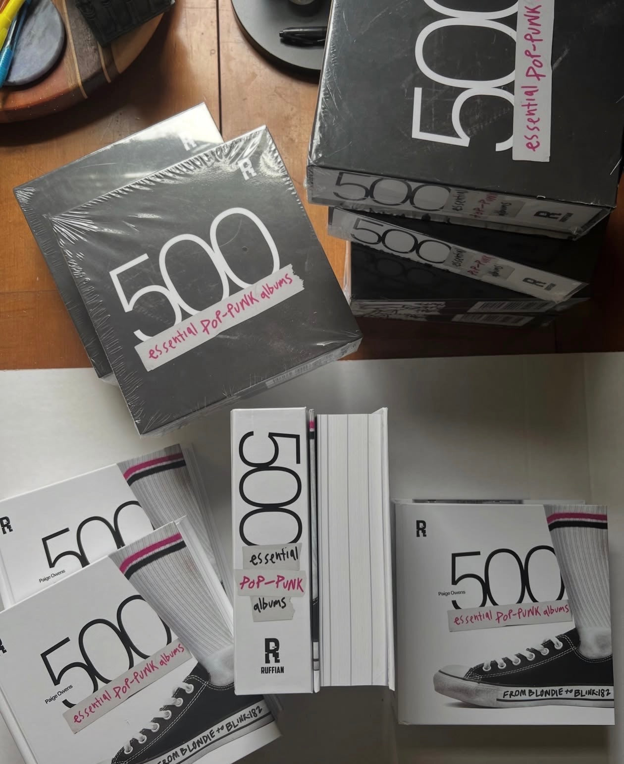 500 Essential Pop-Punk Albums books and shrink-wrapped slipcases stacked on a wood table, showing the Chuck Taylor cover and spine