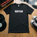 Black Ruffian t-shirt flat lay on wood floor with vinyl records, punk books, and Chuck Taylor sneakers